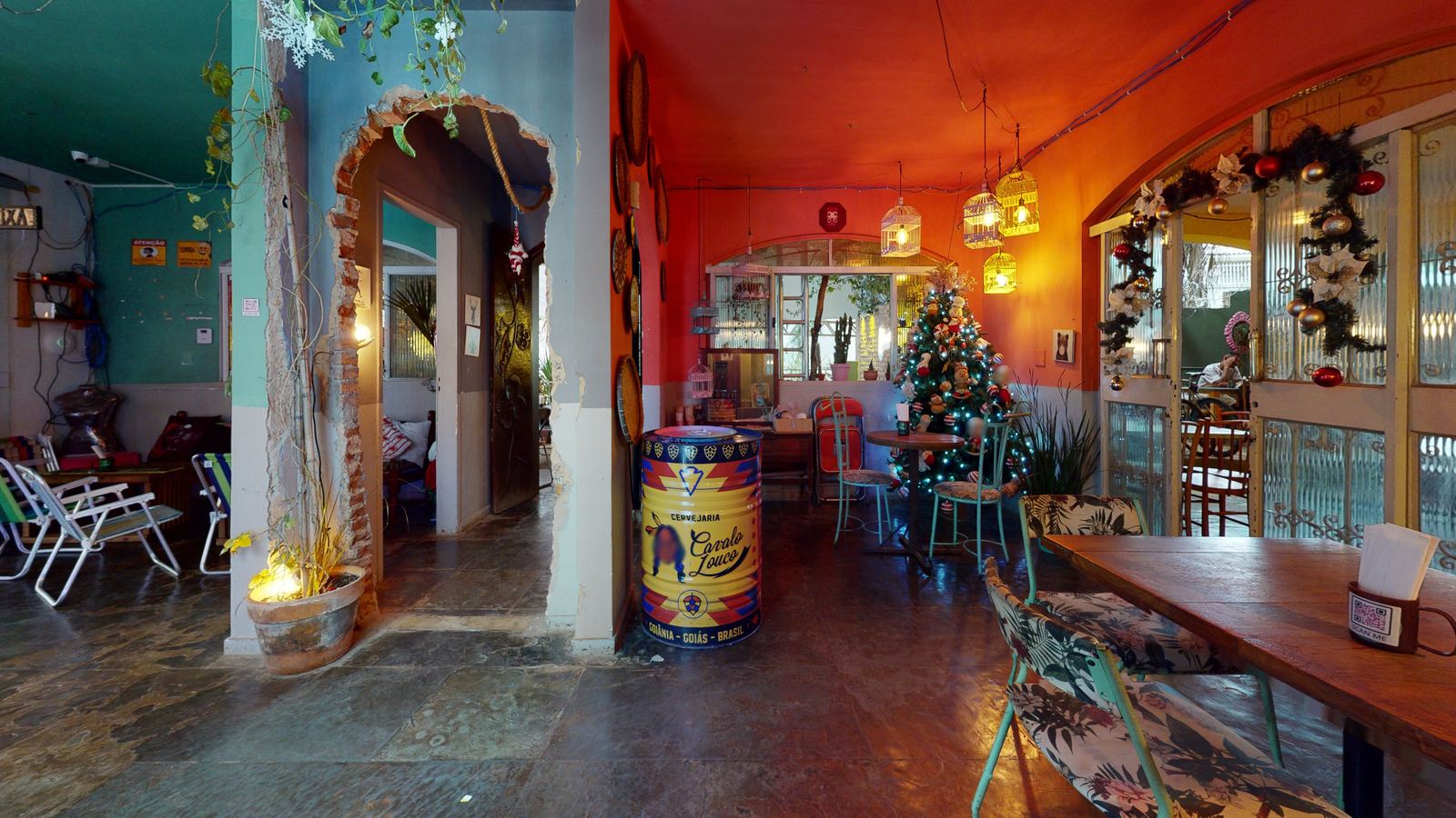 Salão do Mocó Bar, com parede vermelha, bar ao fundo e mesas de madeira, visto de dentro do tour